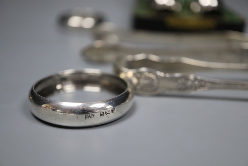 Small silver including a pair of Georgian sugar tongs, cased pepperettes, two napkin rings, spoon, tongs and wine label.